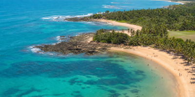 Vista aérea de área litorânea da Bahia com praia, mar e visitantes em cenário ensolarado