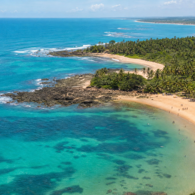 Vista aérea de área litorânea da Bahia com praia, mar e visitantes em cenário ensolarado