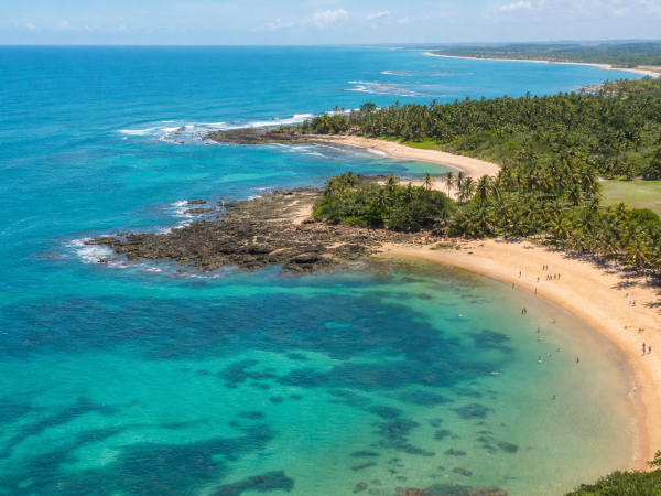 Vista aérea de área litorânea da Bahia com praia, mar e visitantes em cenário ensolarado