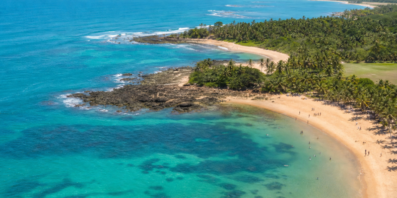 Vista aérea de área litorânea da Bahia com praia, mar e visitantes em cenário ensolarado