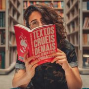 Jovem lê um livro sentada em uma biblioteca, cercada por estantes de livros.