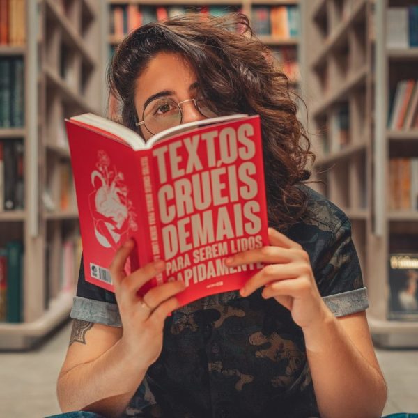 Jovem lê um livro sentada em uma biblioteca, cercada por estantes de livros.