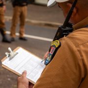 Agente policial escreve em uma prancheta ao ar livre.