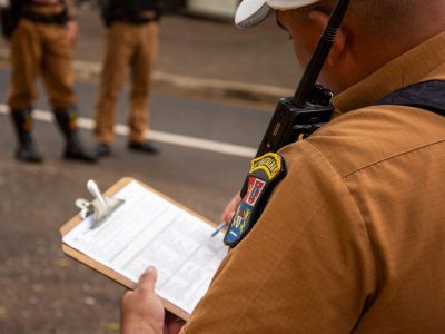 Agente policial escreve em uma prancheta ao ar livre.