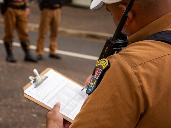 Agente policial escreve em uma prancheta ao ar livre.