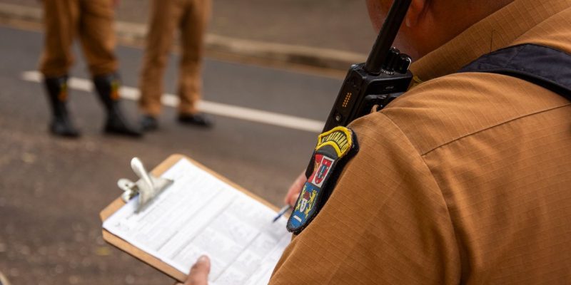 Agente policial escreve em uma prancheta ao ar livre.