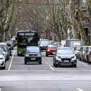 Ônibus do transporte público circula por uma avenida arborizada, entre carros e edifícios.