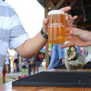 Duas pessoas trocam um copo de cerveja recém-servida ao ar livre, diante de um balcão de bar.