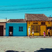 Pessoas caminham diante de construções tradicionais coloridas em um dia ensolarado.