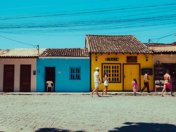 Pessoas caminham diante de construções tradicionais coloridas em um dia ensolarado.